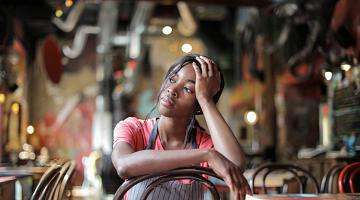 Photo of young restaurant worker sitting alone in empty restaurant, looking concerned 