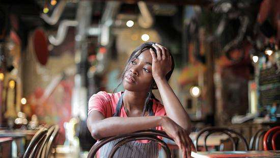 Photo of young restaurant worker sitting alone in empty restaurant, looking concerned 