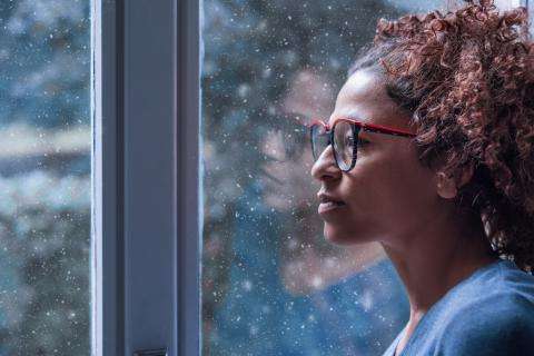 Woman looking out the window pensively, considering whether to disclose her episodic disability